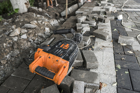 在人行道建筑工程期间 在科布斯通公路上铺设水泥断路器机械男人塞子领班工作服路面人行道活动锤子休息背景图片