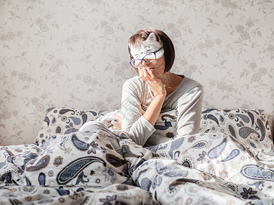 身着灰色睡衣 眼镜和安睡面具的女青年亚麻床单女孩睡眠成人毯子面膜女性宠物背景图片