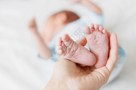 母亲拿着新生婴儿的赤身高跟鞋 小脚在女人手里 在家很舒服白色女士男生妈妈父母儿子蓝色手指投标家庭背景
