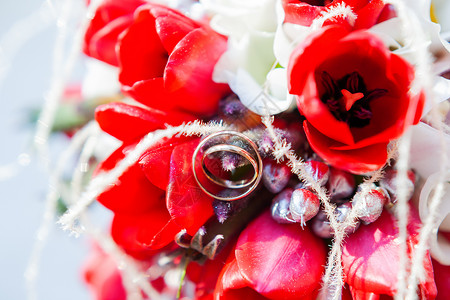 新娘花束上的金色结婚戒指 鲜红郁金香花的爱情和婚姻的象征作品红色订婚阳光宏观郁金香传统珠宝背景图片