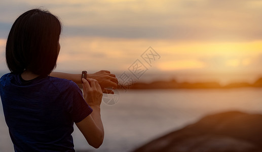 背对背看亚洲女人在跑步后触摸智能乐队背景图片