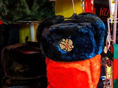 带耳罩的彩色俄罗斯冬帽 带有俄罗斯双头鹰标志的金属别针 纪念品商店在莫斯科 俄罗斯纹章季节双头店铺红色帽子耳垂背景图片