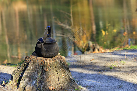 挑着水桶在一片森林湖的背景下 在露天的一块古老树桩上架着金属烧焦的水壶背景