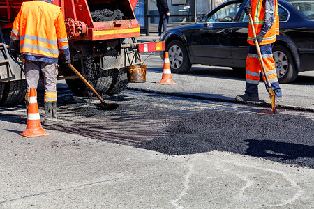 公路工人正在用新鲜沥青修补路段的一段路面上高清图片