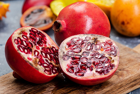 热带水果在木制板上半切果汁食物石榴种子红色背景图片