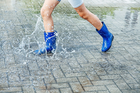 女孩穿着蓝色橡皮靴 在雨后在水坑里跳橡皮街道靴子女性季节孩子跳跃下雨乐趣衣服背景