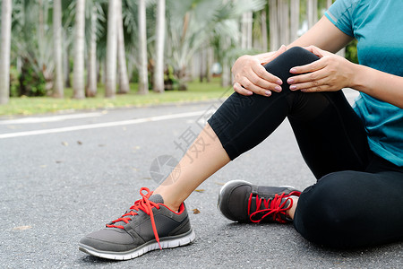 身体健康的女性运动员在膝盖上感到疼痛 户外锻炼运动身体韧带伤害女孩慢跑者跑步肌肉痛苦扭伤蓝色背景图片