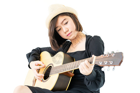 坐在她手里并弹吉他吉他民歌的妇女原声吉他手青少年帽子音乐女性成人女士乐器音乐家背景图片