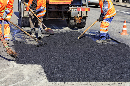 职场道路在修复公路时 工作组用手铲铲平热沥青和铲子工具铺路碎石职业团队男人劳动道路职场建筑工人背景