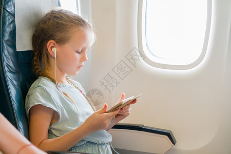 音乐沙龙可爱的小孩 在飞机窗户旁边有笔记本电脑的孩子 Coote kid座位闲暇旅游耳机游客染色玩具沙龙童年电影背景