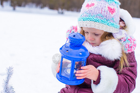 可爱的小可爱女孩在冬天 用蓝灯笼的蜡烛温暖她的手围巾乐趣童年女性微笑婴儿外套手套蓝色雪花背景图片