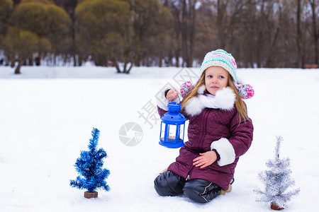 在美丽的冬季雪日 可爱的小女孩在户外守着圣诞灯笼天气手套季节乐趣孩子外套蓝色婴儿女儿微笑背景图片