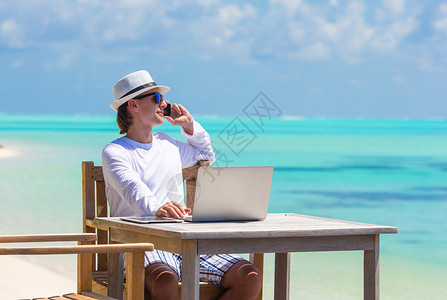 热带海滩上带平板电脑和手机的青年男子商务幸福海洋旅行记事本闲暇工作男性成人展示背景图片