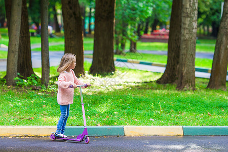 可爱的小女孩 在户外摩托车上玩得开心公园假期婴儿运动享受叶子代步车孩子乐趣闲暇背景图片