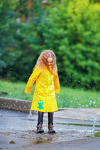 穿黄色雨衣的小女孩穿雨衣和靴子的小女孩 在户外的雨中玩背景