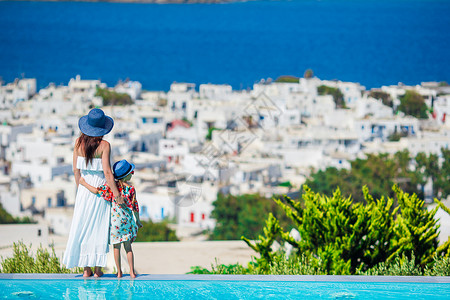 圣洁母亲教会在希腊Cyclades的 游泳池背景希腊小镇边上的可爱小女孩和年轻妈妈背景