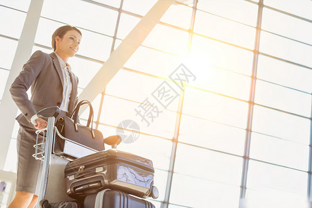 年轻有吸引力的女商务人士驾驶行李车在机场办理报到手续飞机场手提箱大车女士女性手提习俗人士视图托运背景图片
