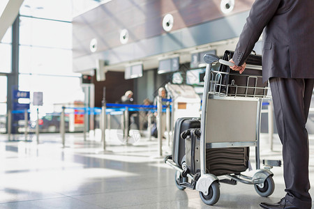 成熟的商务人士在机场办理行李车托运手续 报到检查商业飞机习俗大车游客套装手提箱会议男人背景图片