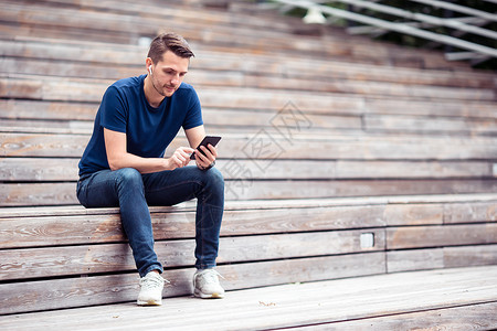 男人在公园散步时正在看手机上的短信 而男子则在公园里走动连接新闻4g大学耳机用法拿铁游客应用程序娱乐背景图片
