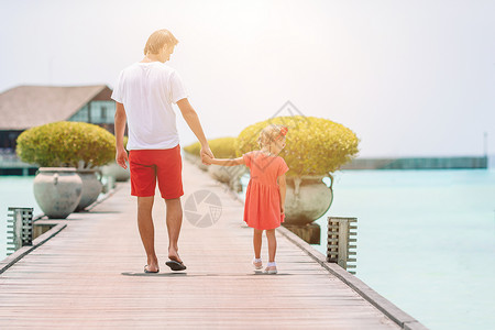 小女孩和爸爸在木制码头上 在异国度假胜地水小别墅附近海岸线男性父亲母亲海洋幸福平房成人海岸假期背景图片
