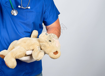 穿蓝色制服和白乳胶手套的医生 戴棕色衣帽玩具医师男人从业者病人儿科医院检查疾病康复背景图片