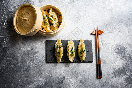 蒸食木蒸锅和黑石板上的煮热中国饺子 在灰色石头纹理的桌子背景顶视图上背景
