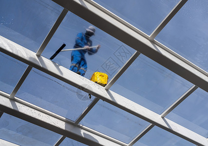 在游泳池上打扫大玻璃屋顶的工人洗涤剂办公室肥皂家政清洁工顶灯服务男性阳光建筑背景图片