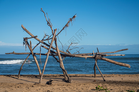 在海滩上漂浮木结构背后的冲浪冲浪者木头框架海滨波浪废料海岸日出阳光环境背景