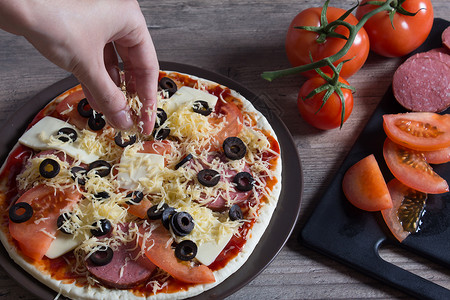 手在比萨上洒奶酪 披萨加西红柿 橄榄和橄榄背景图片