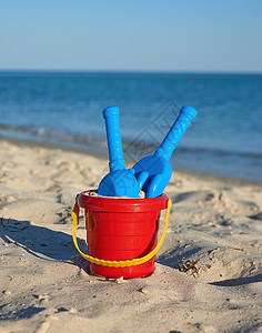 海滩上带沙和铲子的红色婴儿塑料桶晴天游戏闲暇童年塑料玩具黄色假期乐趣孩子背景图片
