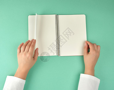 女性用手握着带干净白床单的张开螺旋笔记本背景图片