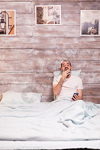 疲累的男人躺在舒适的床上就寝白色时间手机电话卧室长椅互联网枕头房间背景图片