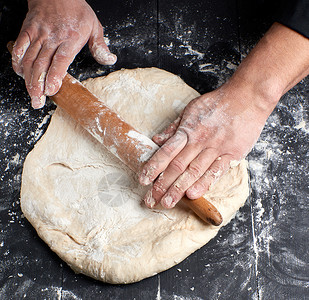 厨师在黑色外衣上 为圆披萨卷钱面团面包师面包营养美食食物桌子厨房面粉白色背景图片
