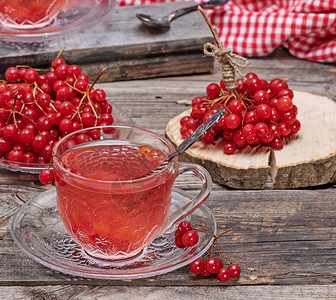 在透明杯子里的热生茶 手柄和碟子饮料桌子荚蒾水果浆果芳香飞碟勺子果汁玻璃背景图片