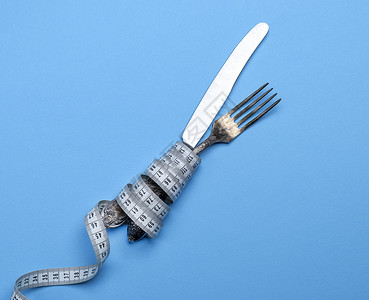 用测量胶带包裹的铁叉和刀重量损失银器白色蓝色节食磁带概念桌子食物背景图片
