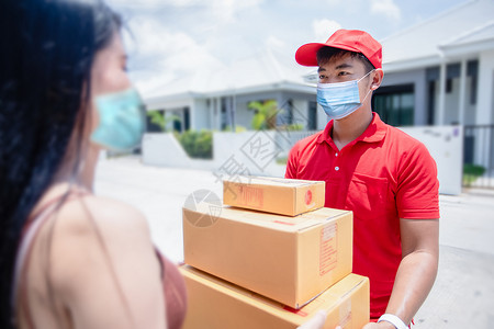 废弃口罩处理身穿红色制服 头戴红色帽子和面罩的亚洲送货员处理纸板箱 送给屋前的女顾客 网上购物和快递背景
