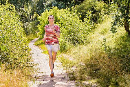 森林慢跑在森林中奔跑的年长女子乐趣运动员赛跑者活动跑步老年运动农村树木人行道背景