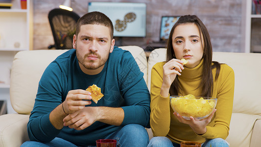 一边看电视 一边吃垃圾食品 一对害怕的夫妇客厅男朋友电视男人情侣胡须男长椅电影女性沙发背景图片