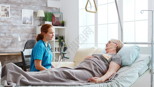 插管退休养老院护士与躺在医院床上的一位老妇人交谈治疗成人说谎男性男人老年病房女士医生药品背景