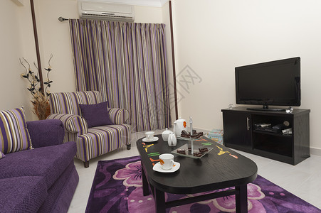 在豪华公寓的休息室蛋糕紫色电视软垫客厅茶几家具房间长椅房子背景图片