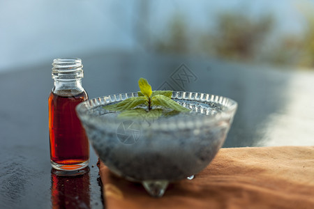 薄荷精华玻璃碗里装满浸泡过的 sabja 种子或 falooda 种子或甜罗勒种子 其提取的精华或精油放在木质表面的透明玻璃瓶中蔬菜荷叶背景