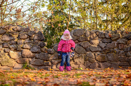 身着冬衣的小女孩站在石墙背景上高清图片
