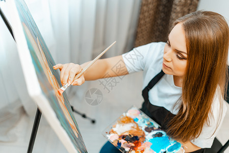 创意职来职往字体艺术艺术家的作品 年轻漂亮的女孩艺术家画一幅画 艺术家的工作室 创意的过程 绘图和油漆 艺术家的库存 特写教育刷子画架蓝色画家职背景