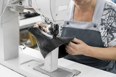 皮革车间的缝纫机在用手处理鞋子的皮革细节 在鞋厂 老妇人的手拿着缝纫机压缩机械衣服机器行动裁缝工具拉链工作商业背景图片