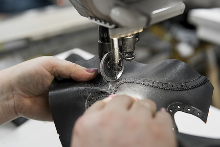 皮革车间的缝纫机在用手处理鞋子的皮革细节 在鞋厂 老妇人的手拿着缝纫机家具压缩工艺接缝机器工作工具作坊制造业商业背景图片