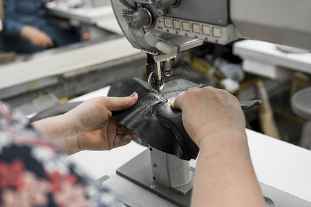 皮革车间的缝纫机在用手处理鞋子的皮革细节 在鞋厂 老妇人的手拿着缝纫机工作金属工厂生产纺织品机械制造业机器压缩缝纫背景