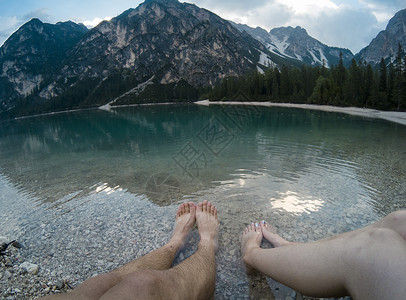 男人和女人的腿反对的壮丽景色 森林和山脉反映在湖水白云岩阿尔卑斯山 意大利 在5 hero5 上拍摄 徒步旅行和冒险帽子男性背包背景