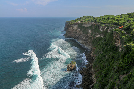 海岸图印度尼西亚巴厘岛的乌鲁瓦图悬崖与凉亭和蓝色大海的景色 寺的美丽风景 白天有五颜六色的鲜花前景 高悬崖风景秀丽的沿海景观太阳地平线背景