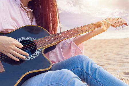 沙滩上音乐家女人的手弹着音响吉他 在日落时在沙滩上用手指捕捉和弦女性音乐音乐会娱乐细绳乐器词曲吉他手音乐家艺术家背景