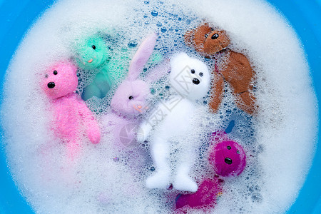 玩具兔子在洗衣洗涤剂水中用熊玩具 浸泡的兔子娃娃身体垫圈粉末黑发盆地蓝色搪瓷篮子洗衣店衣夹背景
